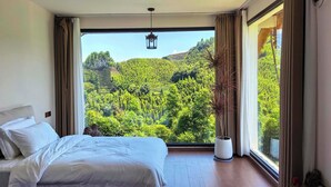 A bedroom with a large window offering a view of a lush green forest and hills. - Shanye Lianglu (Leshan)