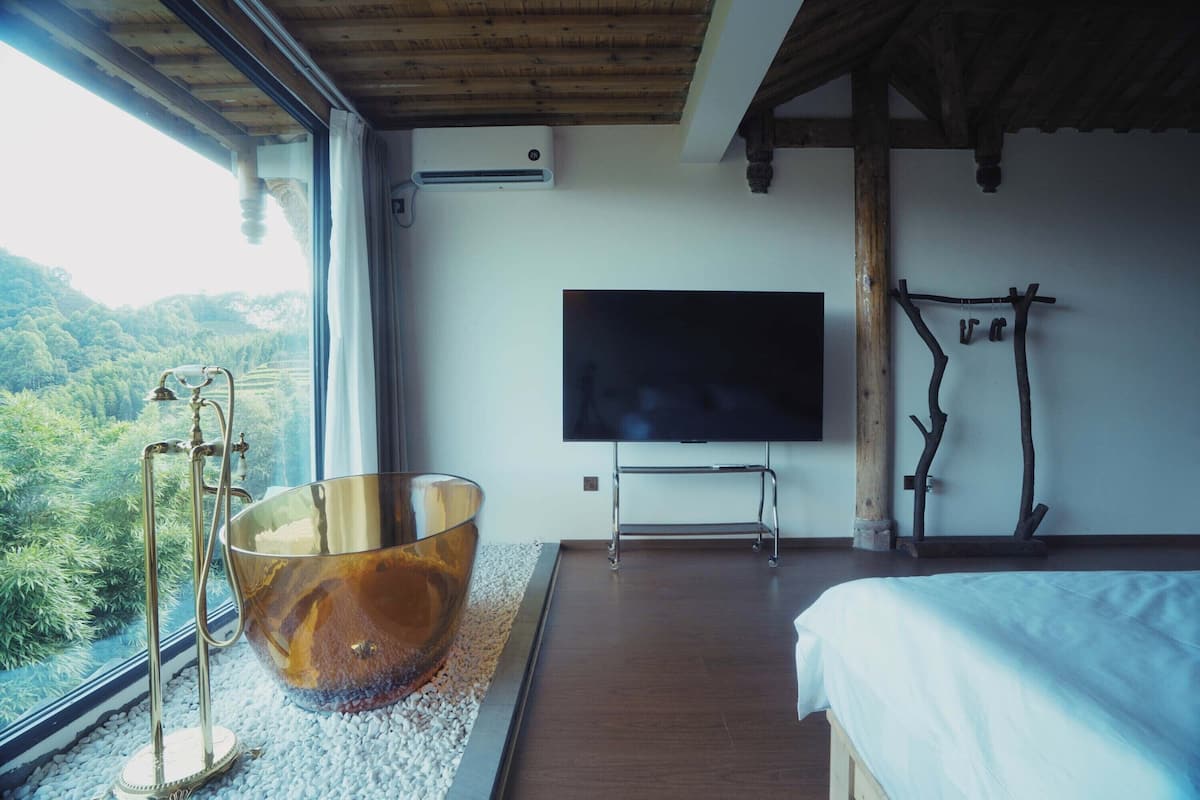 A bedroom with a large window, a flat-screen TV, a wooden bed, and a unique glass bowl centerpiece.