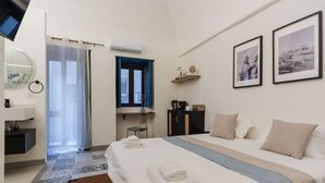 Een hotelkamer met een bed, een bureau, een stoel, een spiegel, een plank met decoratieve objecten en een raam met blauwe gordijnen.
