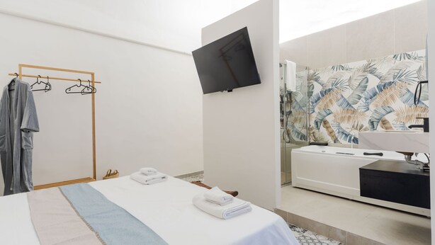 Een moderne hotelkamer met een bed, een aan de muur bevestigde televisie, een douche en een badkamer met een grote spiegel.