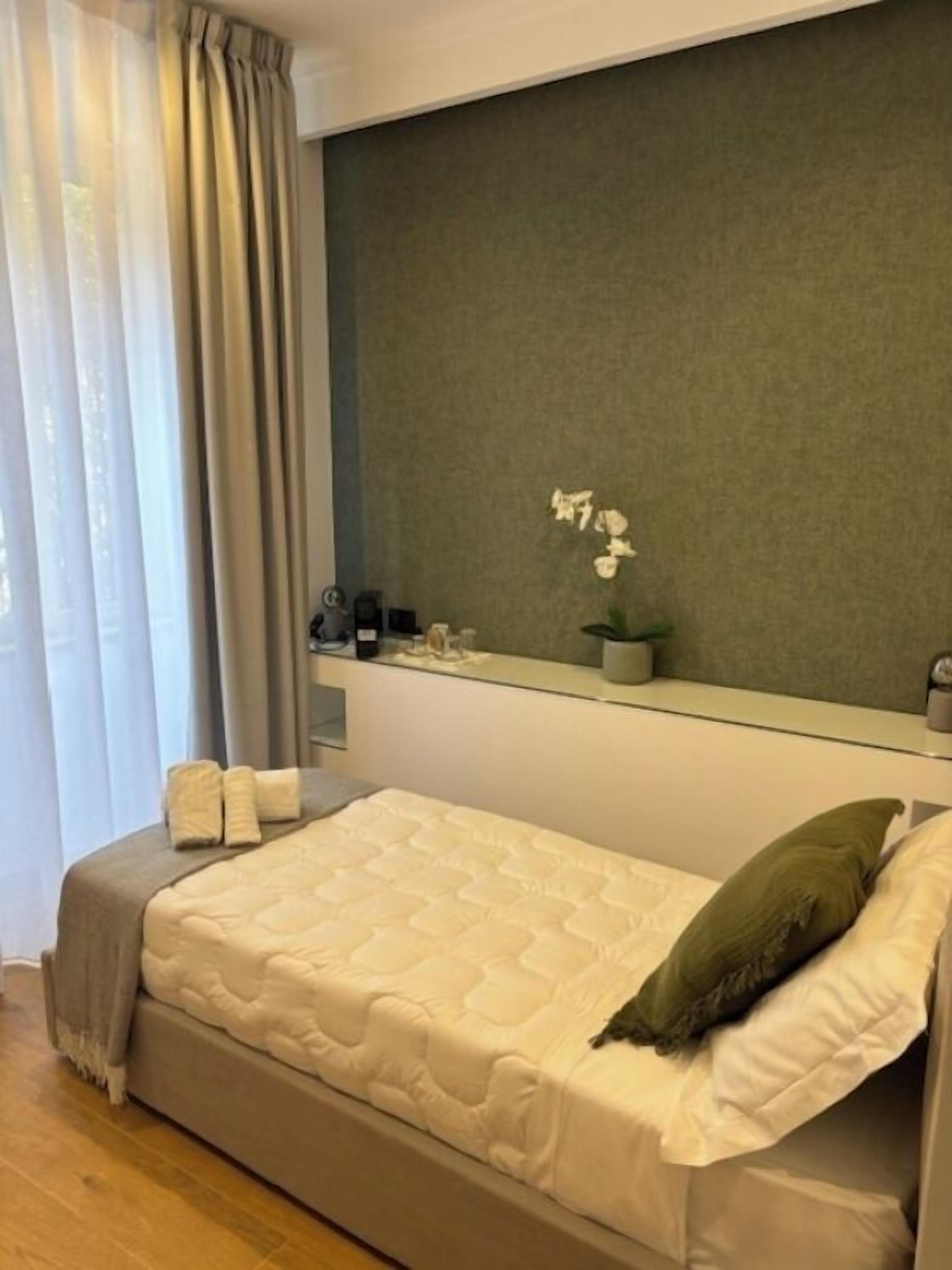 A modern bedroom with a bed, a nightstand, a mirror, and a window with curtains.