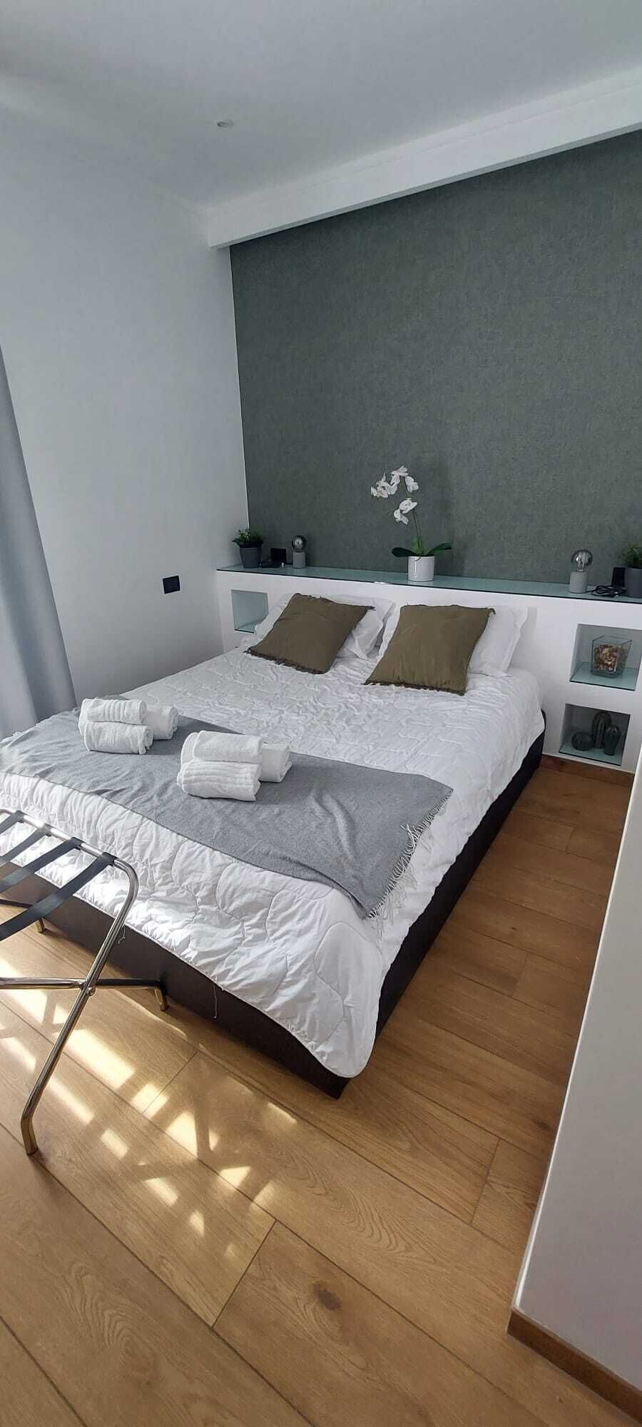 Une chambre moderne avec un grand lit, une table de chevet, une commode, une petite plante en pot et une fenêtre.