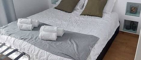 Un dormitorio moderno con una cama grande, una mesita de noche, una pequeña planta en maceta y una ventana.