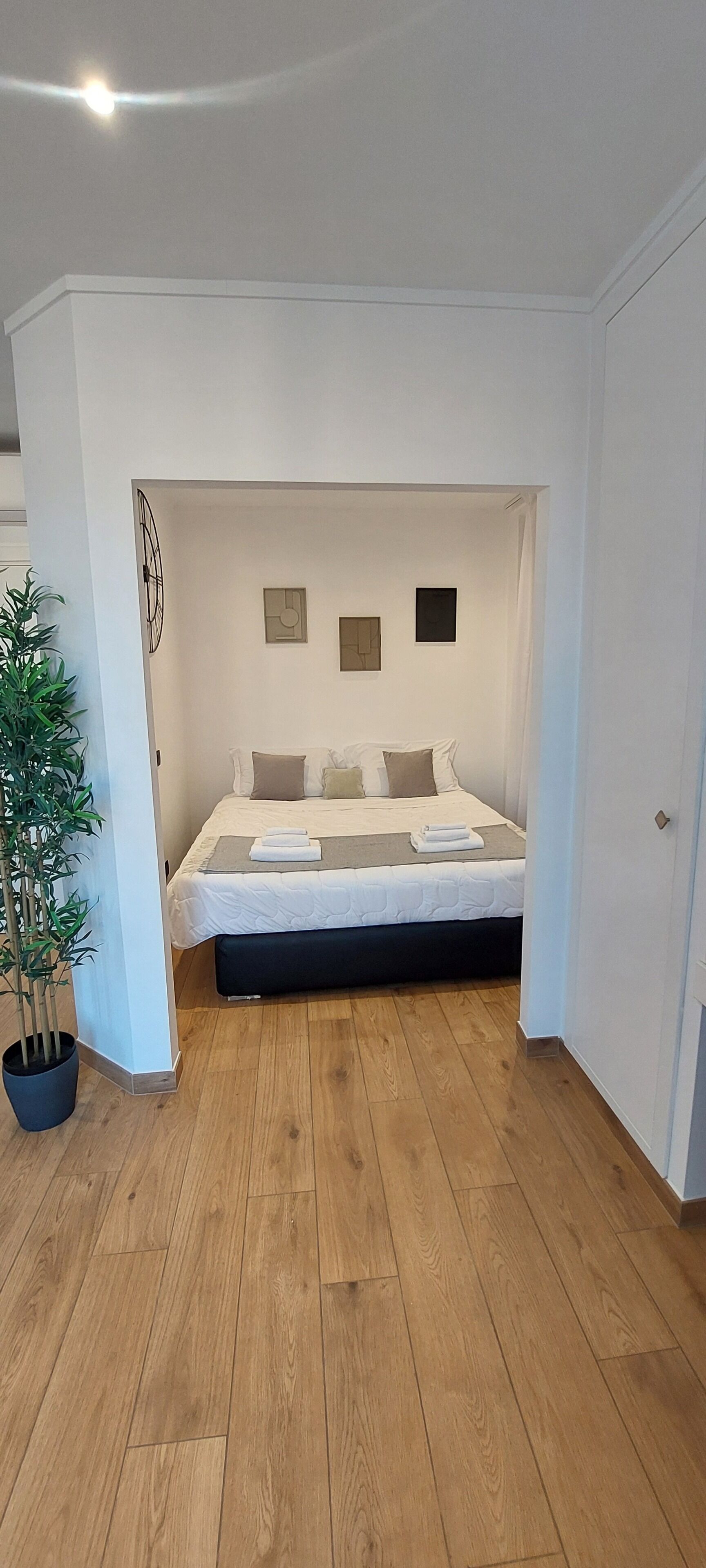 A bedroom with a bed, a potted plant, and artwork on the wall.