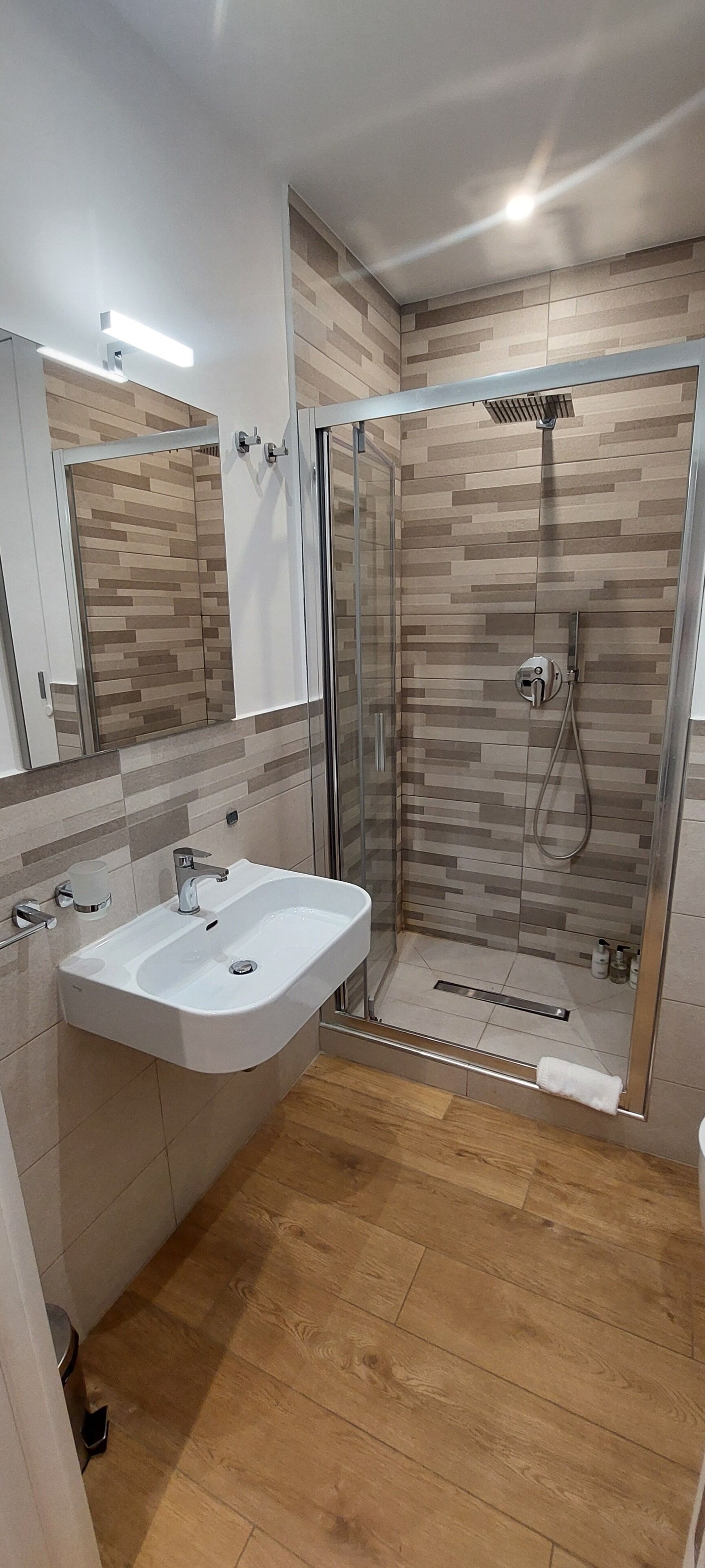 Une salle de bain moderne avec une douche à parois de verre, un lavabo blanc et un plancher en bois.