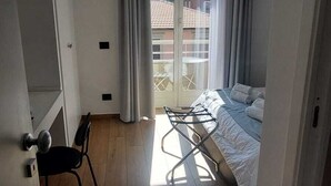 A bedroom with a bed, a chair, a sliding glass door leading to a balcony, and a wooden floor.