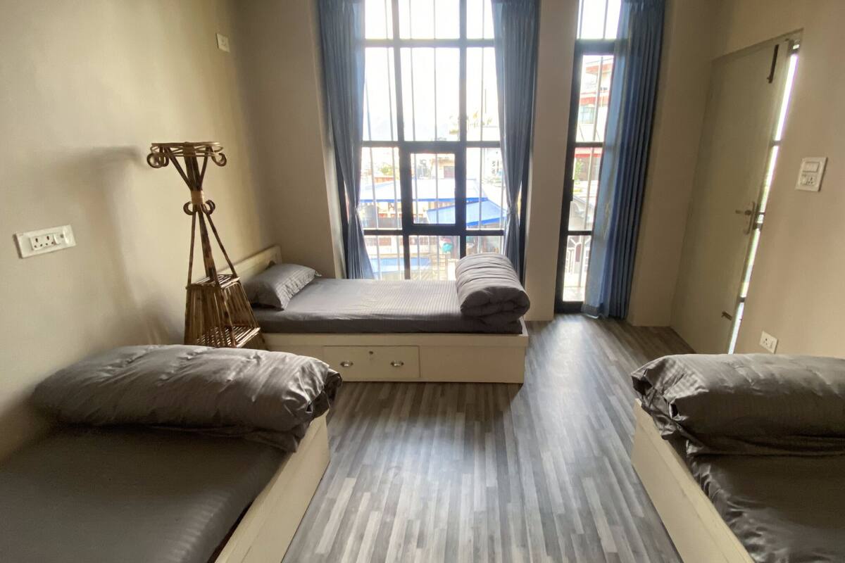 A small, compact room with two single beds, a small table, and a window with curtains.