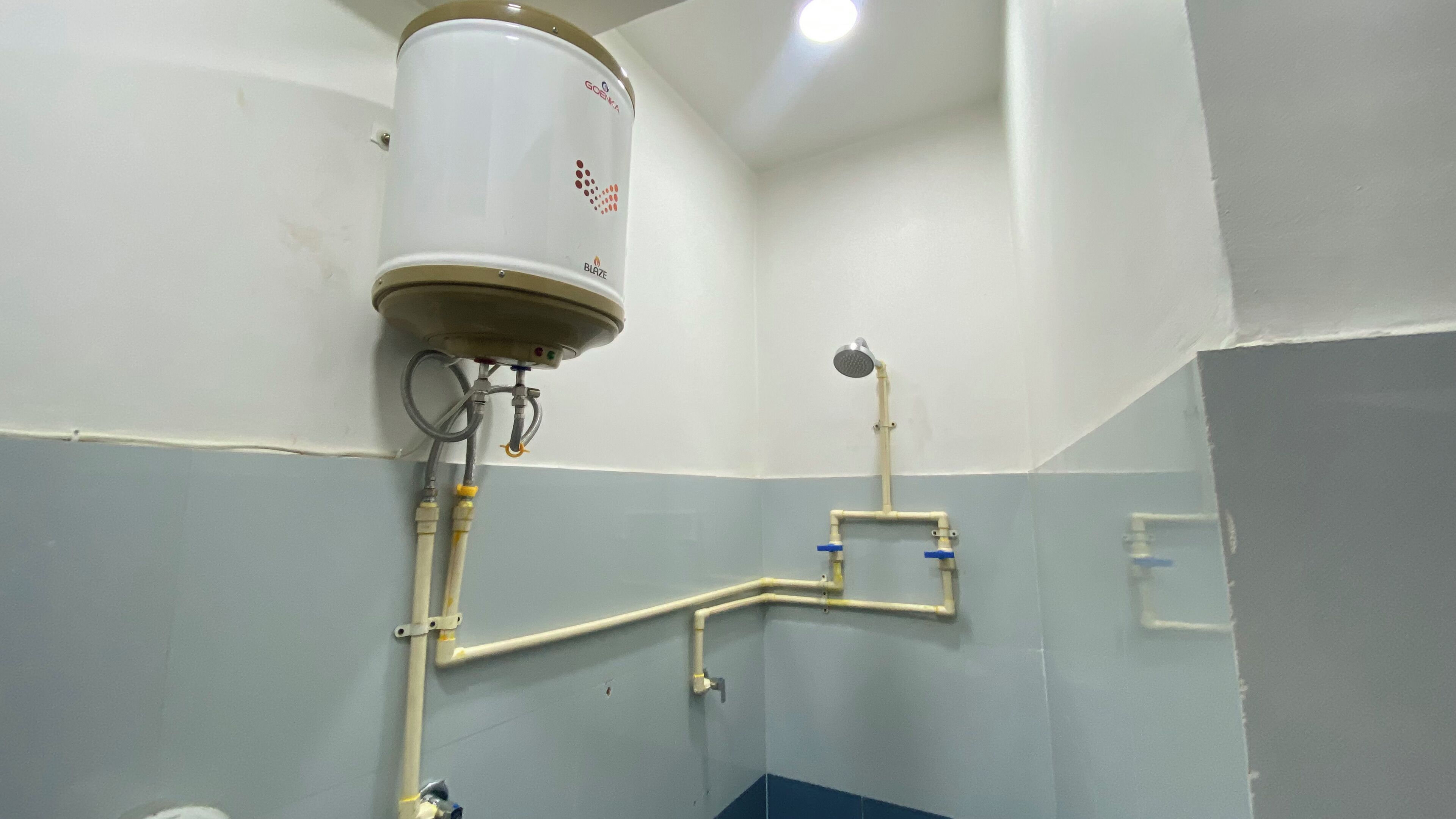 Casa de banho com sanita branca, chuveiro e termoacumulador fixado na parede.