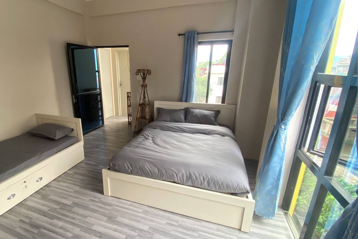 A bedroom with two single beds, a wardrobe, a mirror, and a window with curtains.