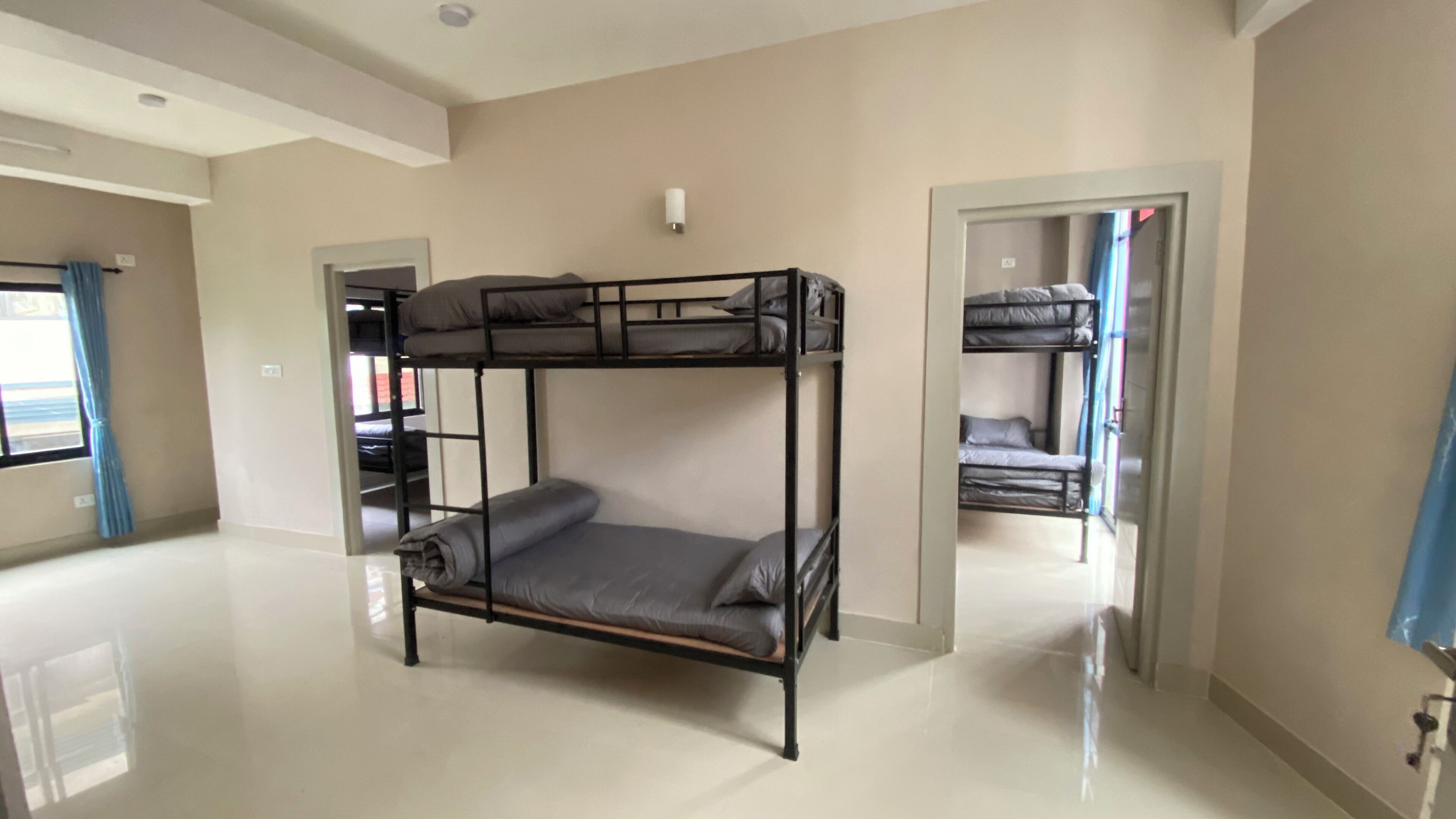 Une chambre avec un lit superposé, une fenêtre, une porte et un luminaire fixé au mur.