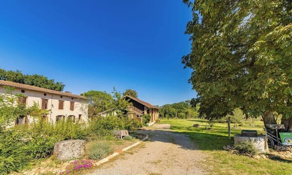 A rural setting with a building, a gravel path, and a grassy area with trees.