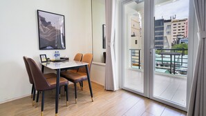 A modern room with a dining table, chairs, a framed picture, and a large sliding glass door leading to a balcony with a view of buildings. - The Rixx Saigon Central - Next to Ben Thanh Market (Ho Chi Minh City)