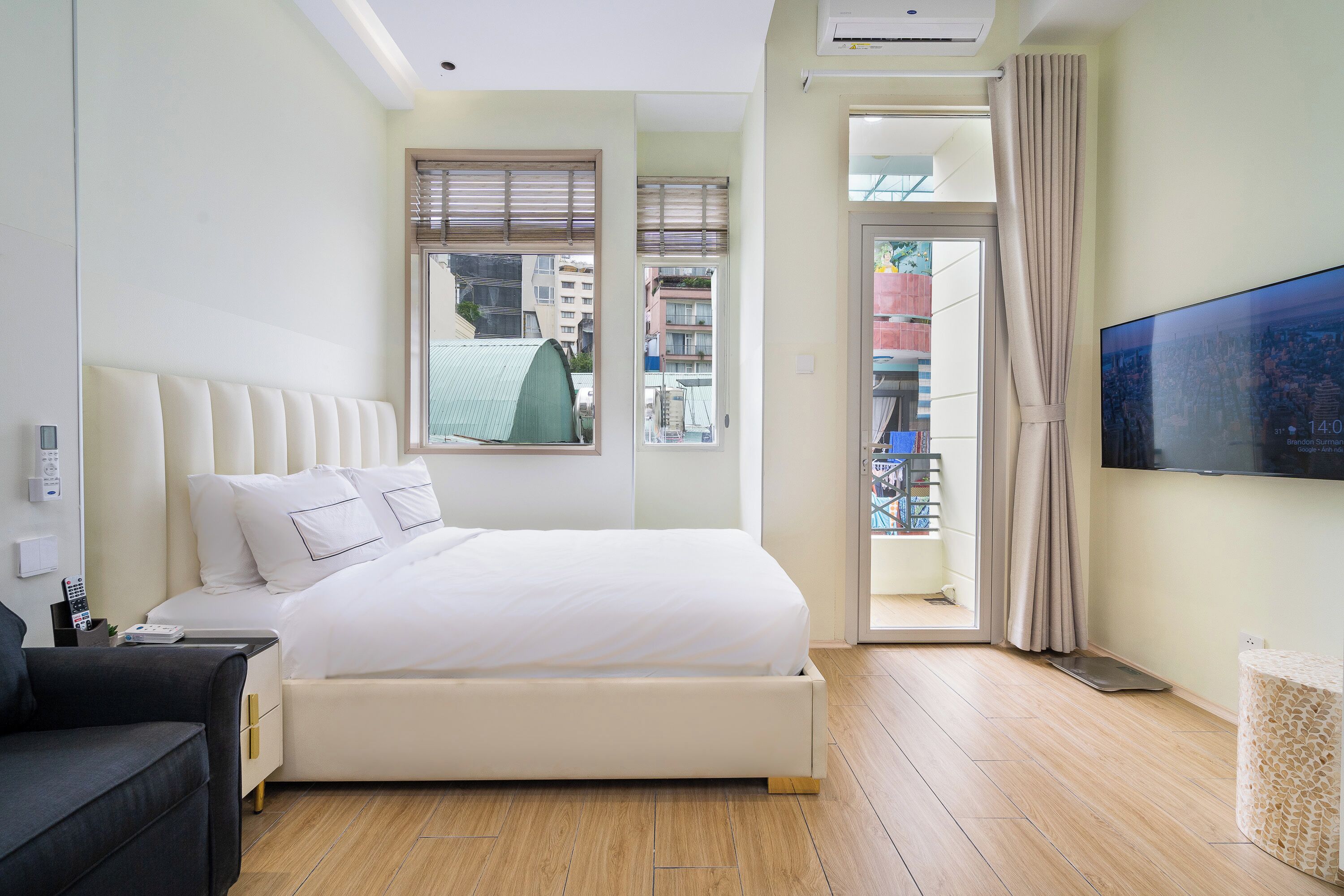 A modern hotel room with a large bed, a flat-screen TV, a sofa, and a view of the city through the window.