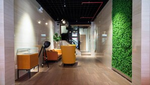 A modern lobby with wooden flooring, yellow armchairs, a glass display case, and a green vertical garden wall. - The Rixx Saigon Central - Next to Ben Thanh Market (Ho Chi Minh City)