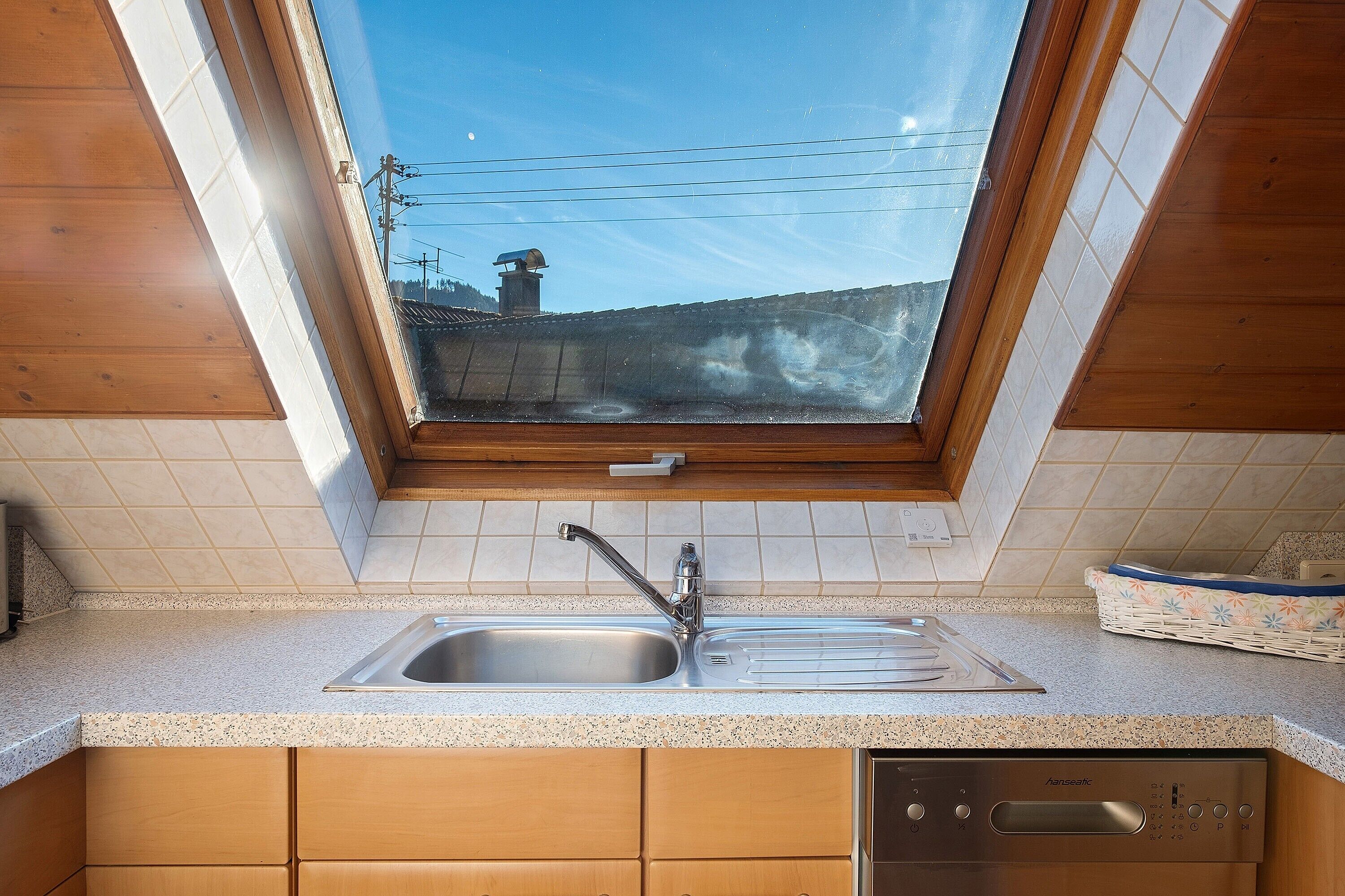 Eine Küche mit Fenster, einem Edelstahl-Spülbecken und Holzschränken.