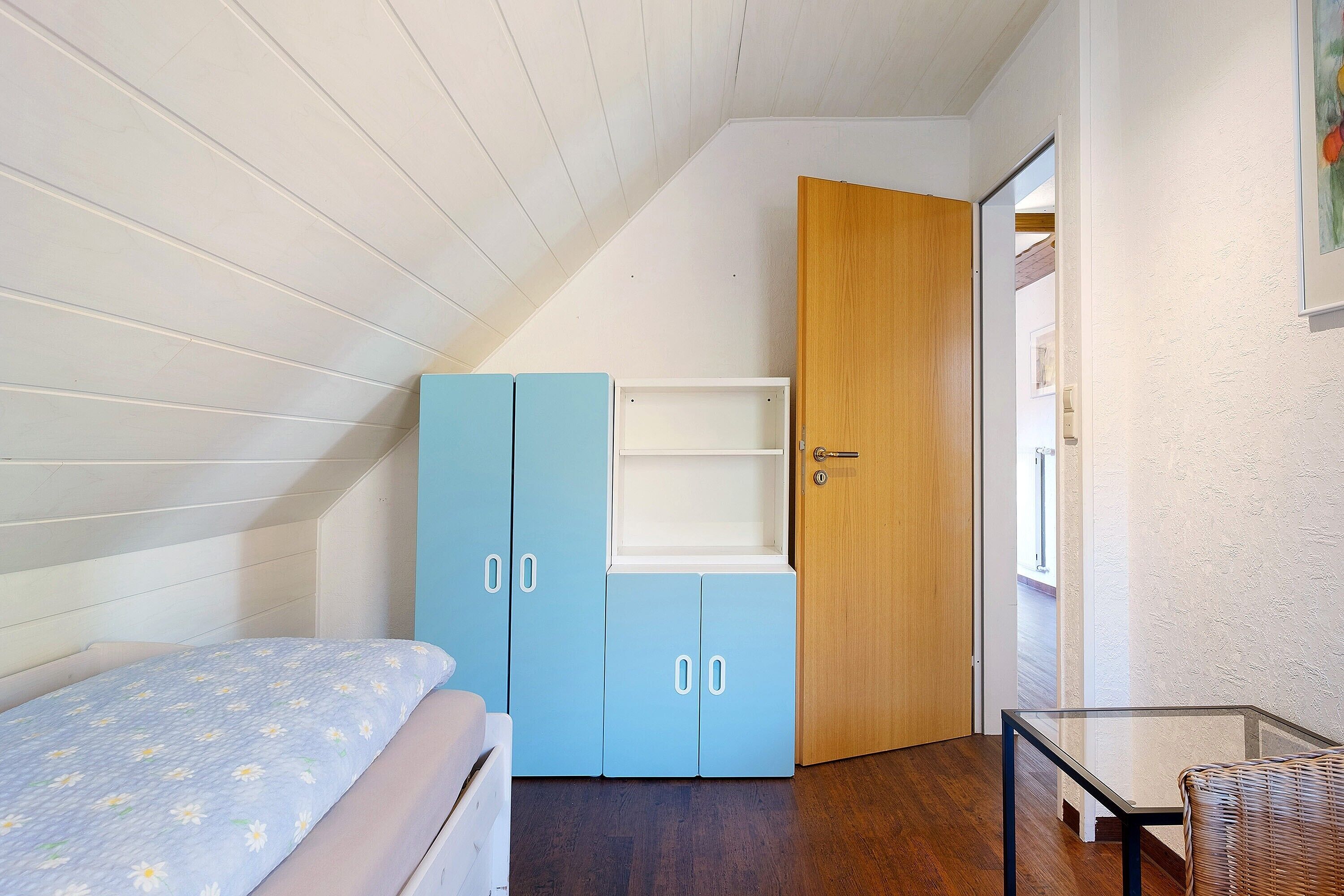 Ein Schlafzimmer mit Bett, Kleiderschrank, Tür und Glastisch.