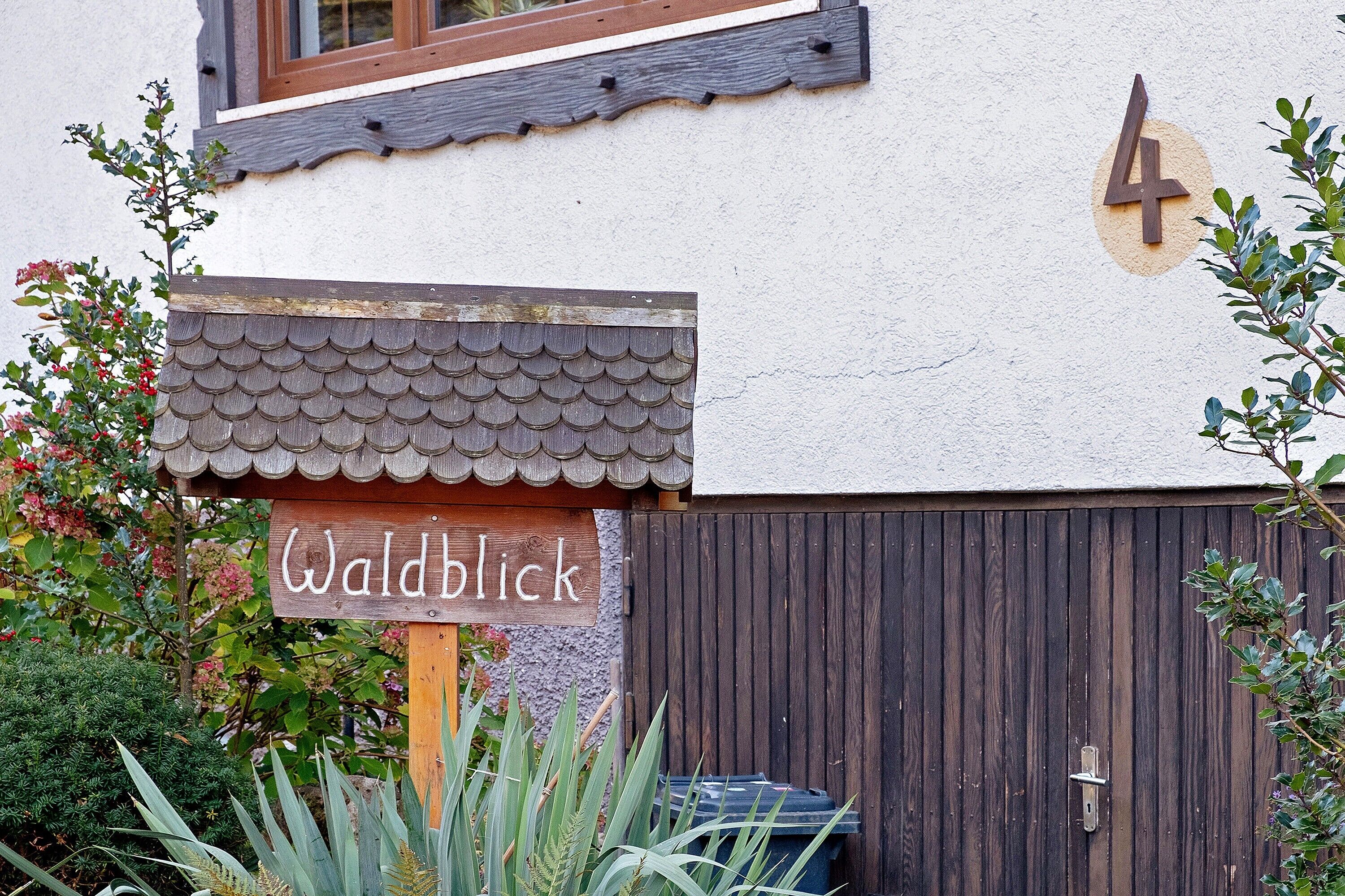 Ein Gebäude mit einem Holzschild, auf dem 'Waldblick' steht, und der Zahl '4' an der Wand.