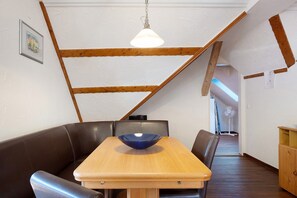Spiseområde med et træbord, polstrede sæder i sort læder, en hængende lampe og synlige træbjælker i loftet.