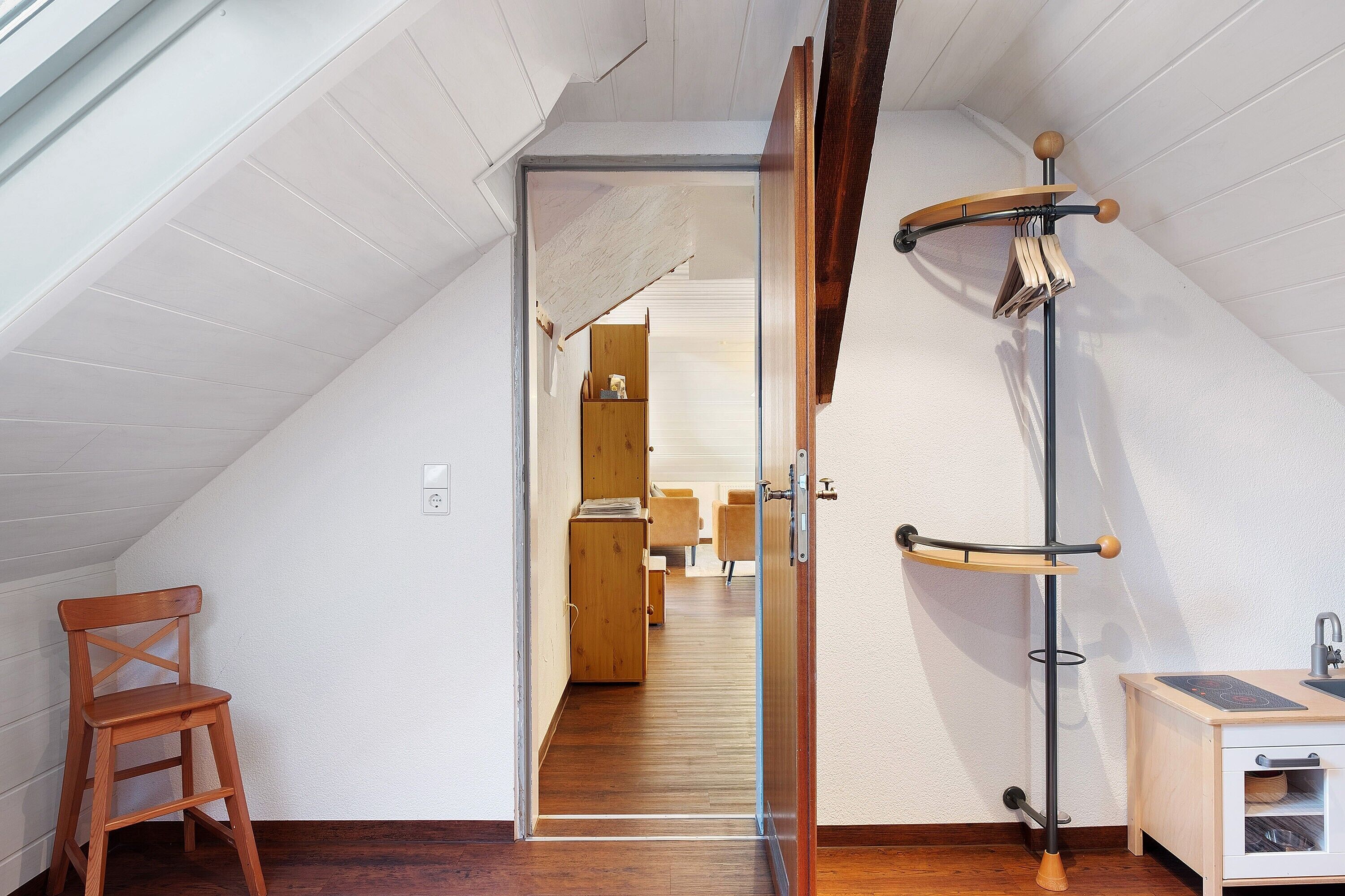 A room with a wooden chair, a coat rack, and a small cabinet.