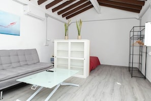 A modern living room with a grey sofa, a glass coffee table, a white shelving unit with plants, and a black metal rack.