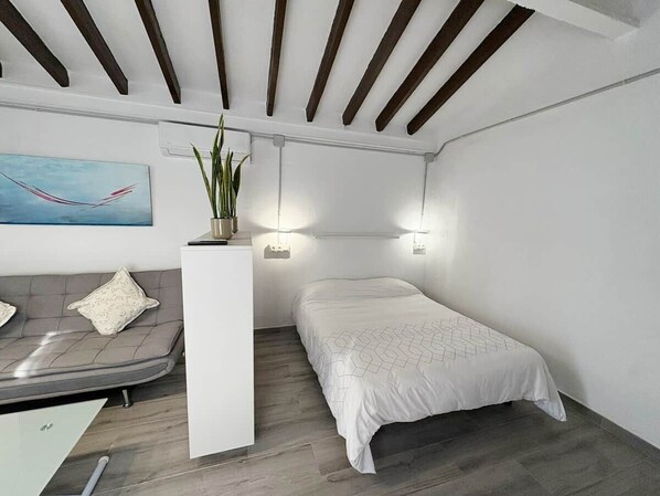 A modern bedroom with a bed, a sofa, a small table, and a potted plant.