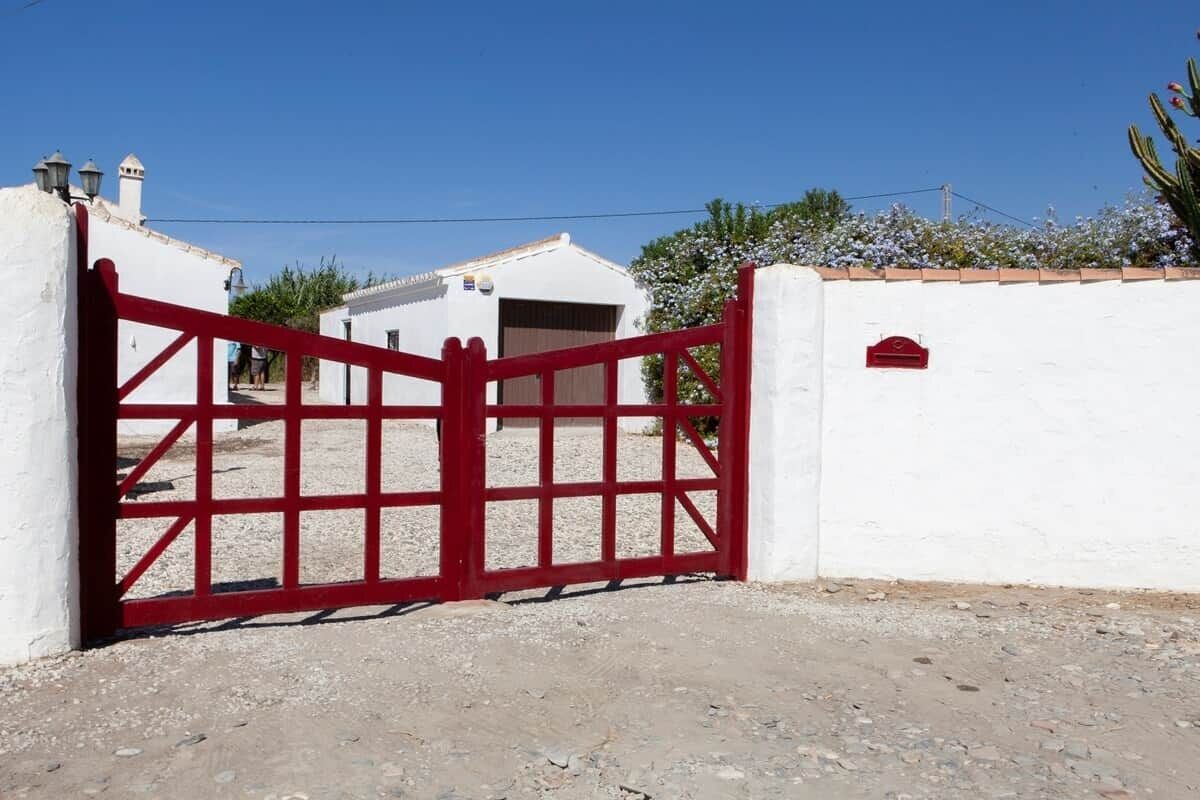 A gated entrance with a red gate, white walls, and a clear blue sky.