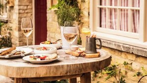 A round wooden table set with plates of food, glasses of white wine, and a metal mug.
