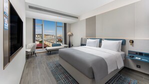 A modern hotel room with a large bed, a seating area with a view, and a flat-screen TV.