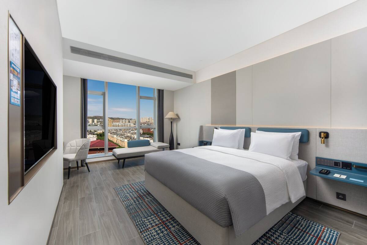 A modern hotel room with a large bed, a seating area with a view, and a flat-screen TV.