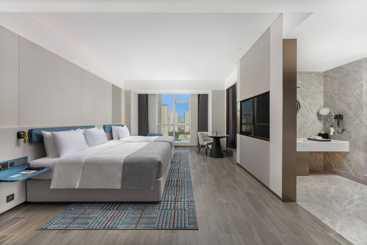 A modern hotel room with a large bed, a desk, a chair, a TV, and a bathroom with a marble wall.