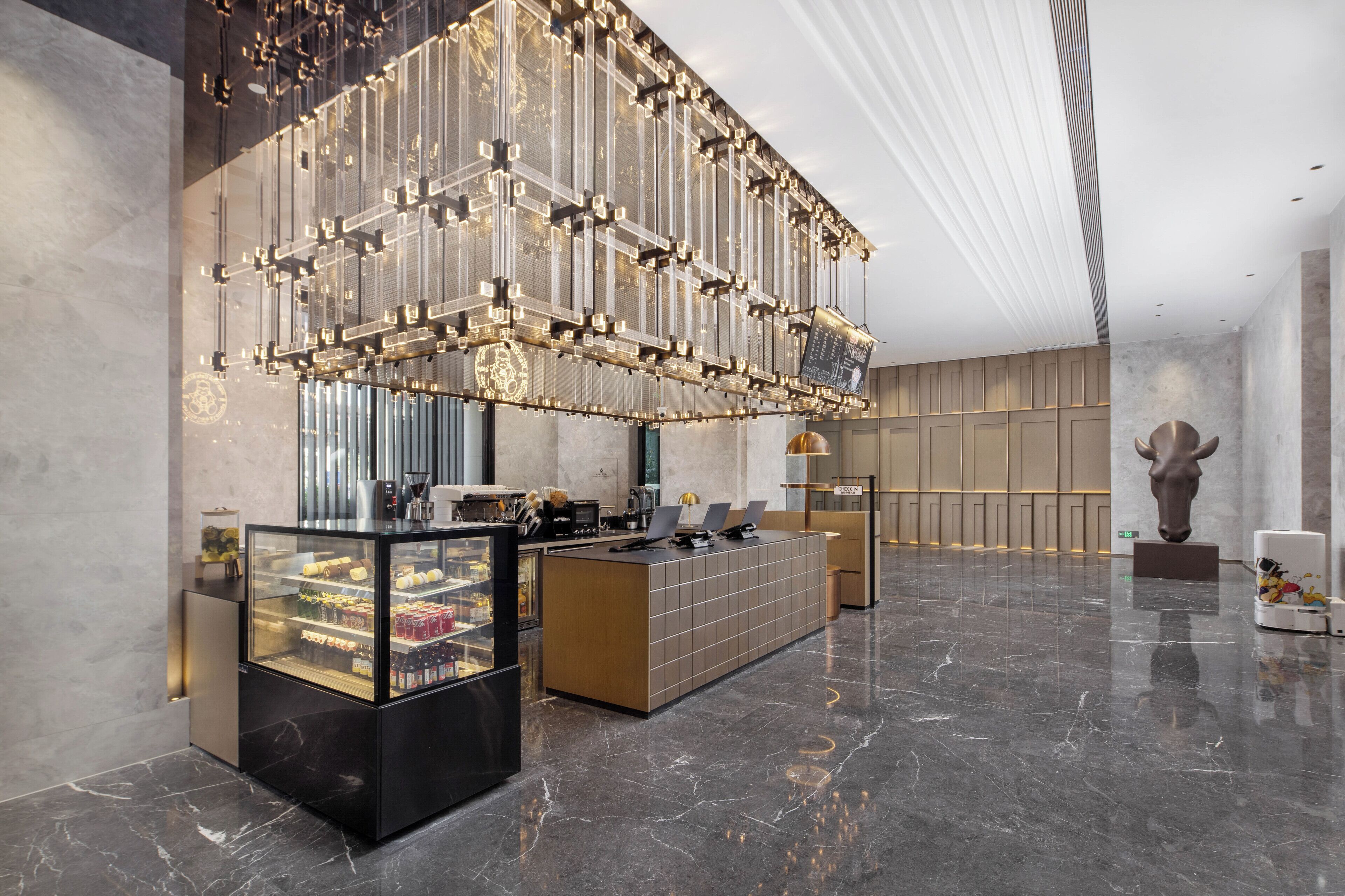 A modern lobby with a reception desk, a refrigerated display case, and a large decorative light fixture.