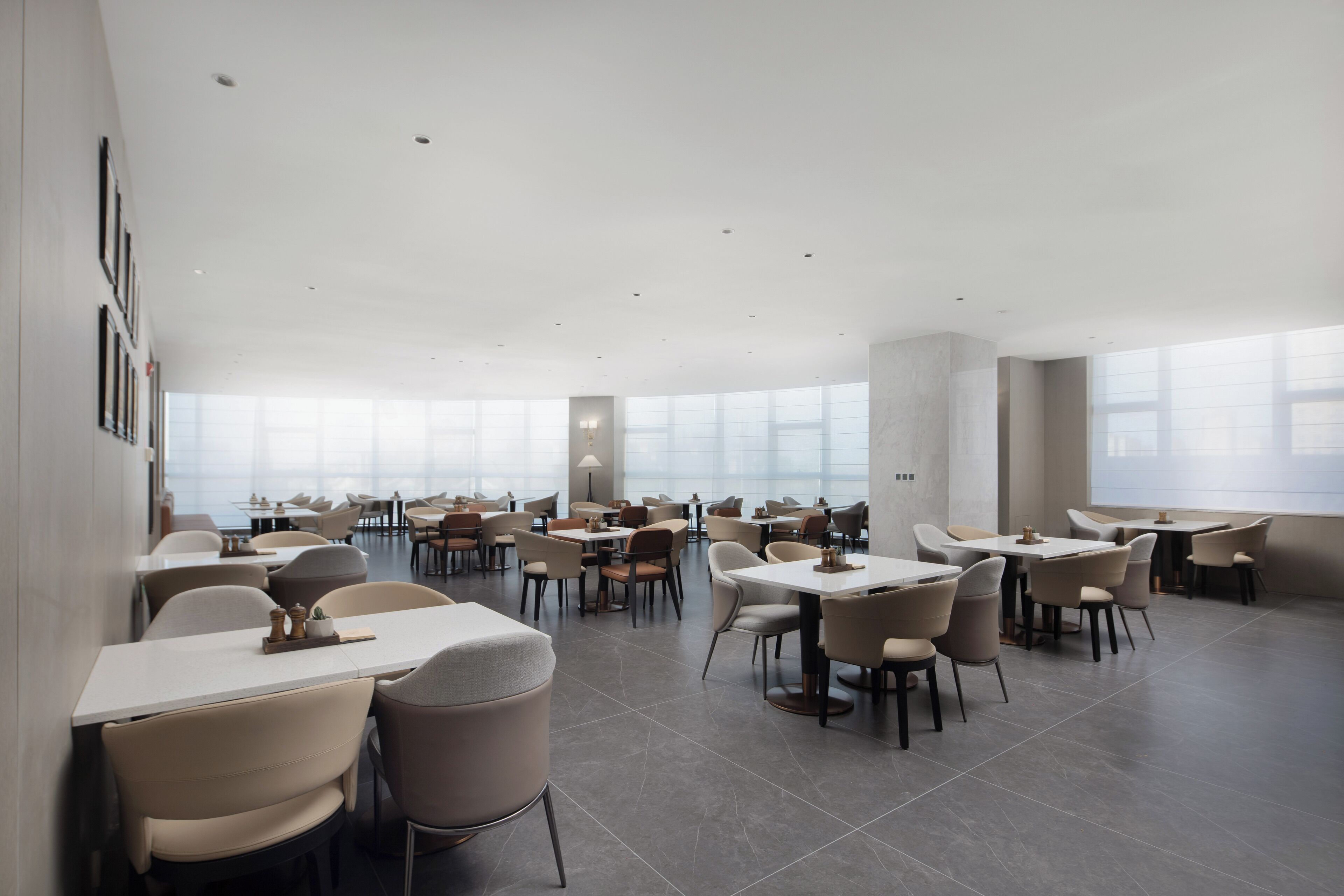 A spacious restaurant with high ceilings and large windows, featuring modern furniture and a clean, minimalist design.