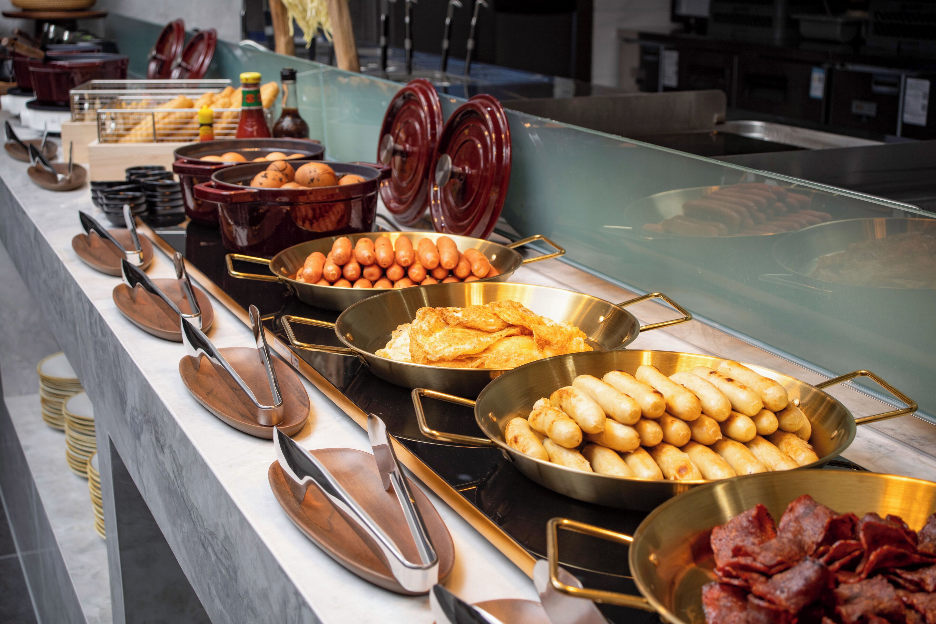 Buffet com diversos alimentos, incluindo ovos mexidos, salsichas e bacon.