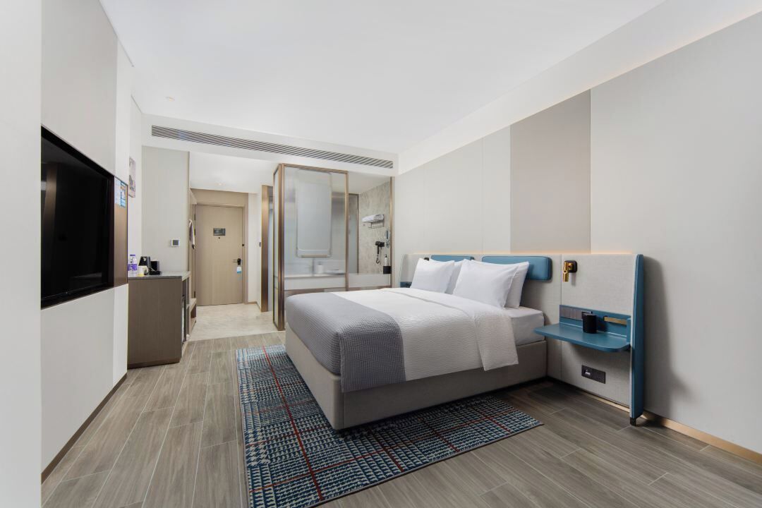 Una habitación de hotel moderna con cama, mesita de noche, televisor y baño visible a través de una puerta abierta.