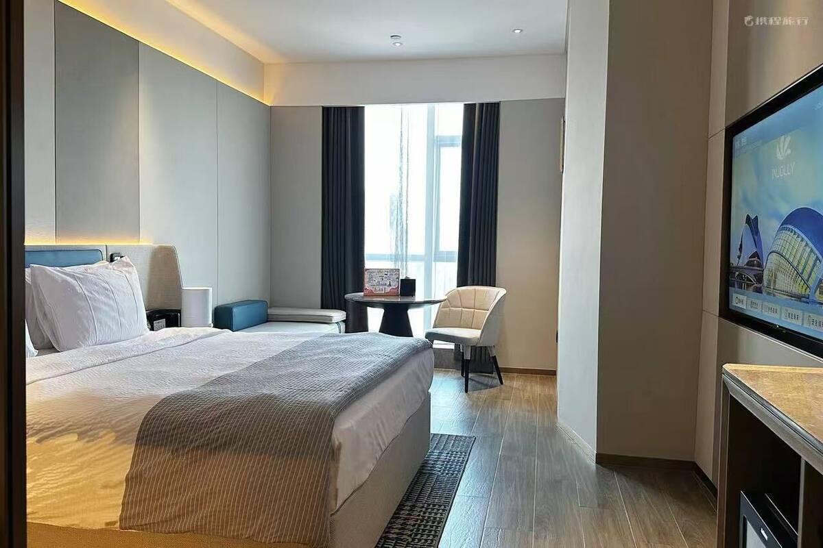 A hotel room with a bed, a desk, a chair, a TV, and a window with curtains.