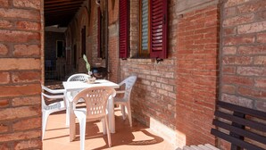 Un bâtiment en briques avec des volets rouges, une table avec des chaises et un banc.