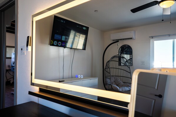 A modern room with a large mirror, a mounted TV, a ceiling fan, and a bed with a unique hanging chair.