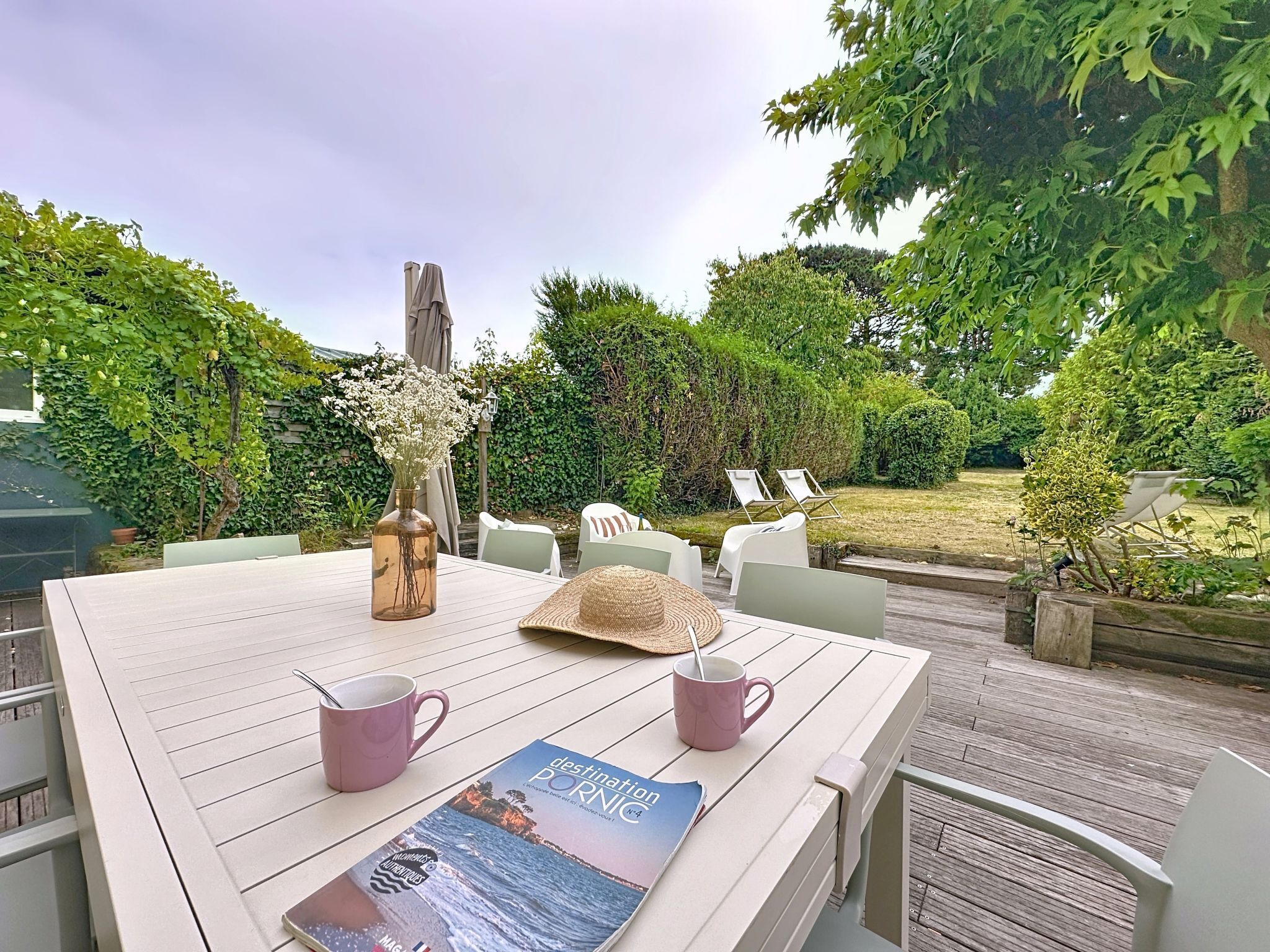Un área de comedor al aire libre con una mesa dispuesta para dos, un jarrón decorativo, un sombrero de paja y una revista de viajes.