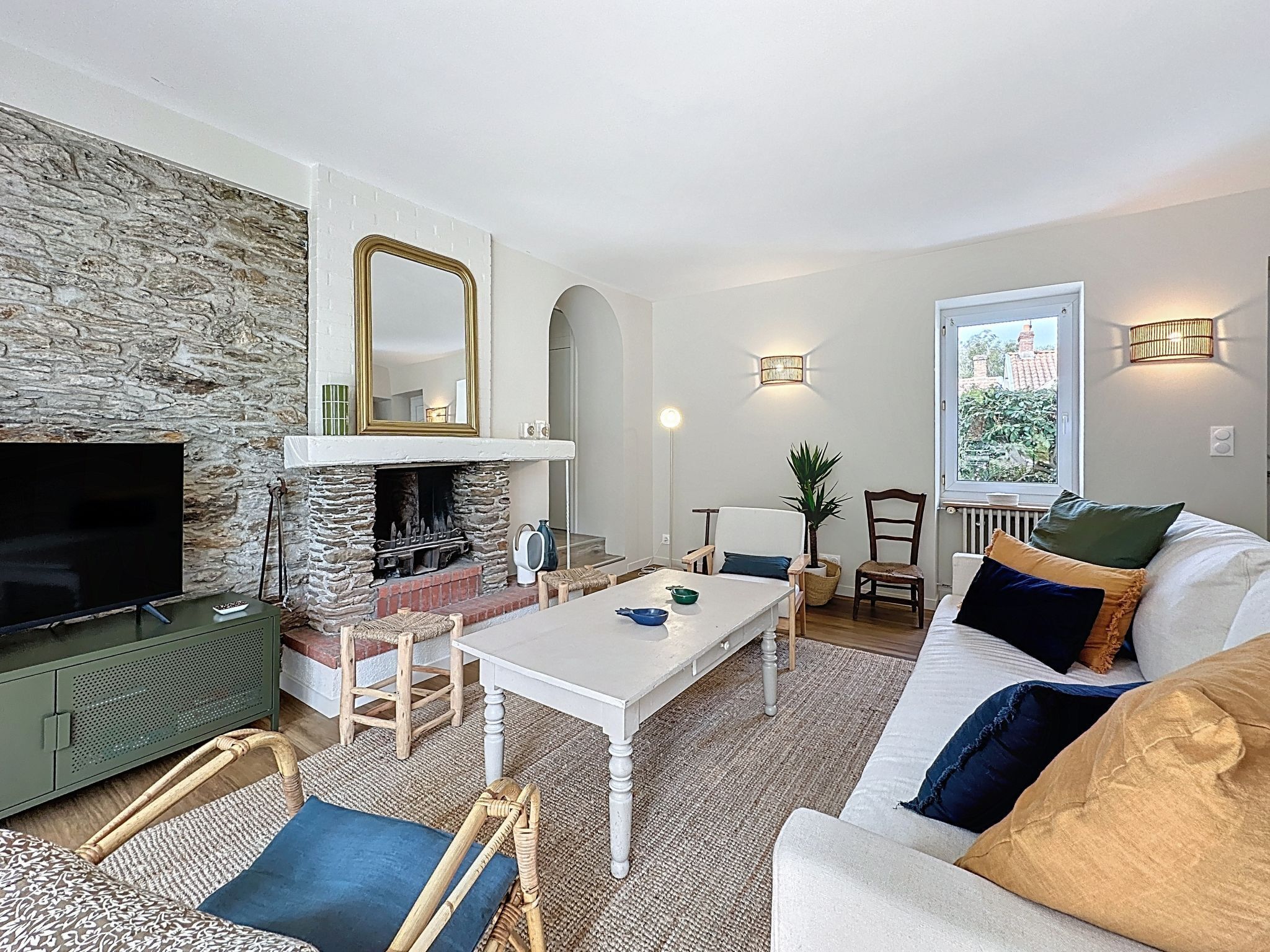 A living room with a stone wall, fireplace, television, white sofa, and a window with a view.