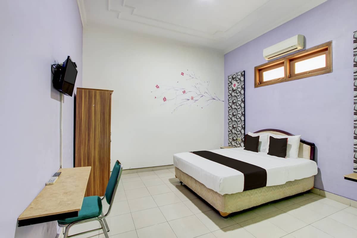 A bedroom with a bed, a desk, and a chair. There is a wall-mounted TV and an air conditioning unit.