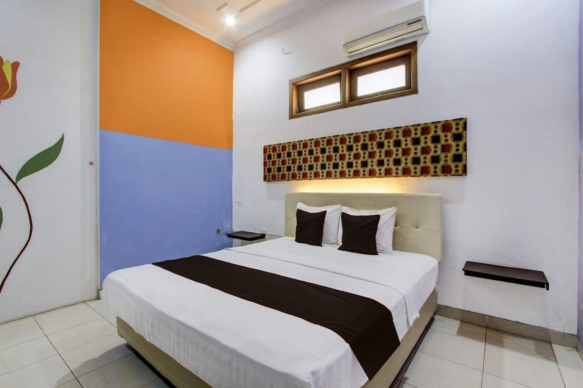 A hotel room with a bed, a nightstand, a wall-mounted air conditioner, and a window with blinds.
