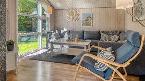 Una habitación acogedora con techo de madera, un sofá gris, un sillón azul y una mesita de café blanca.