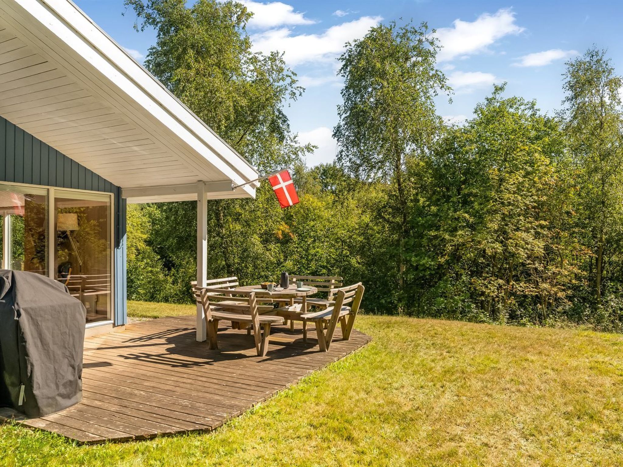 Une terrasse en bois avec une table et des chaises, un drapeau et un bâtiment doté d’un patio couvert.