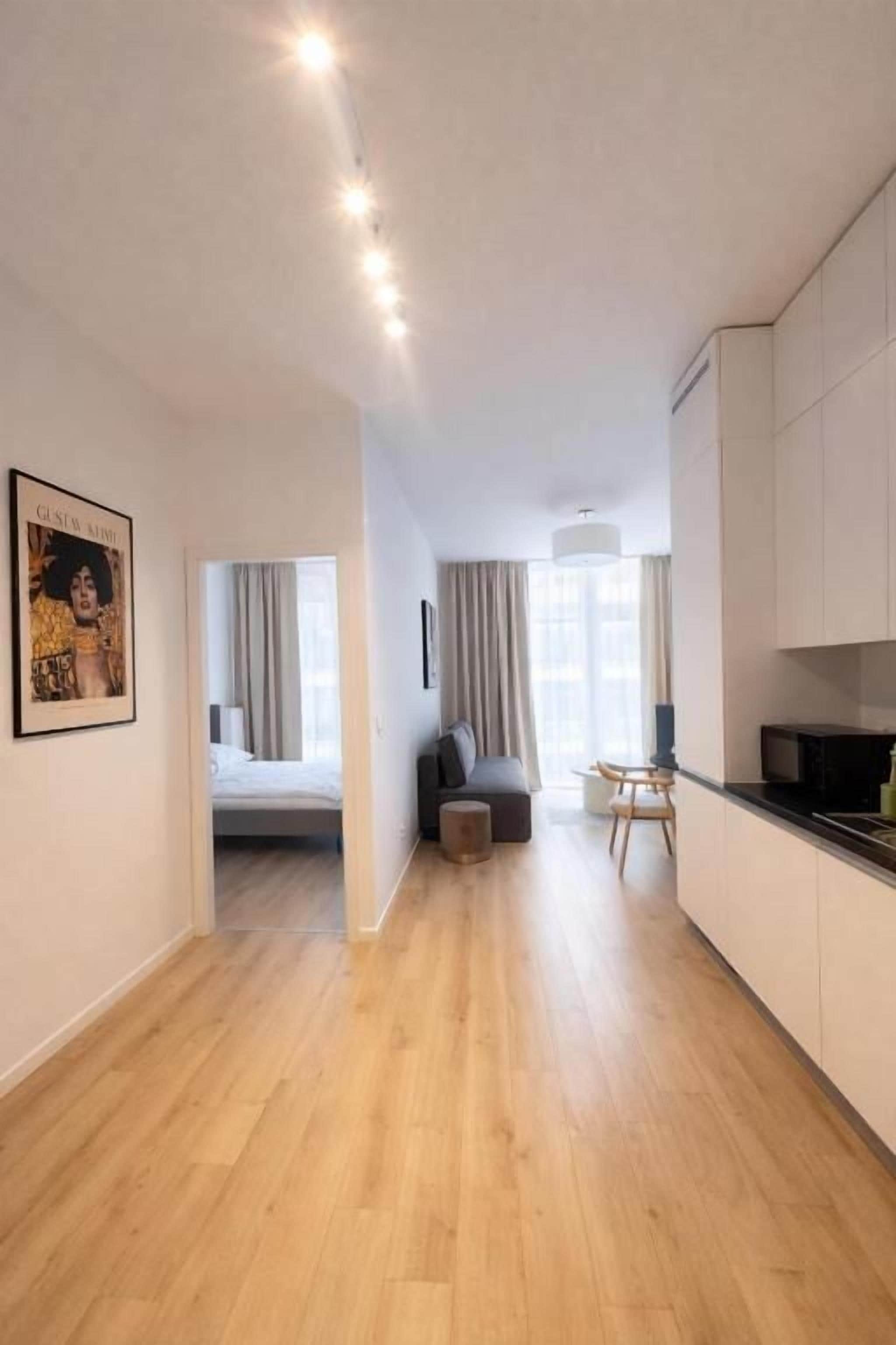 Un apartamento moderno con piso de madera, un comedor con mesa y sillas, una kitchenette y un dormitorio con cama y cortinas.