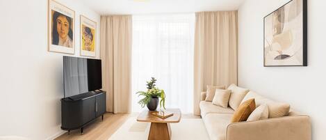 A modern living room with a sofa, a coffee table with a plant, a TV, and artwork on the walls.