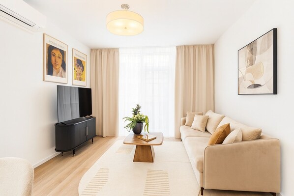A modern living room with a sofa, a coffee table with a plant, a TV, and artwork on the walls. - BROWARY DESIGNER APARTMENTS by Country 2 Country (Warsaw)