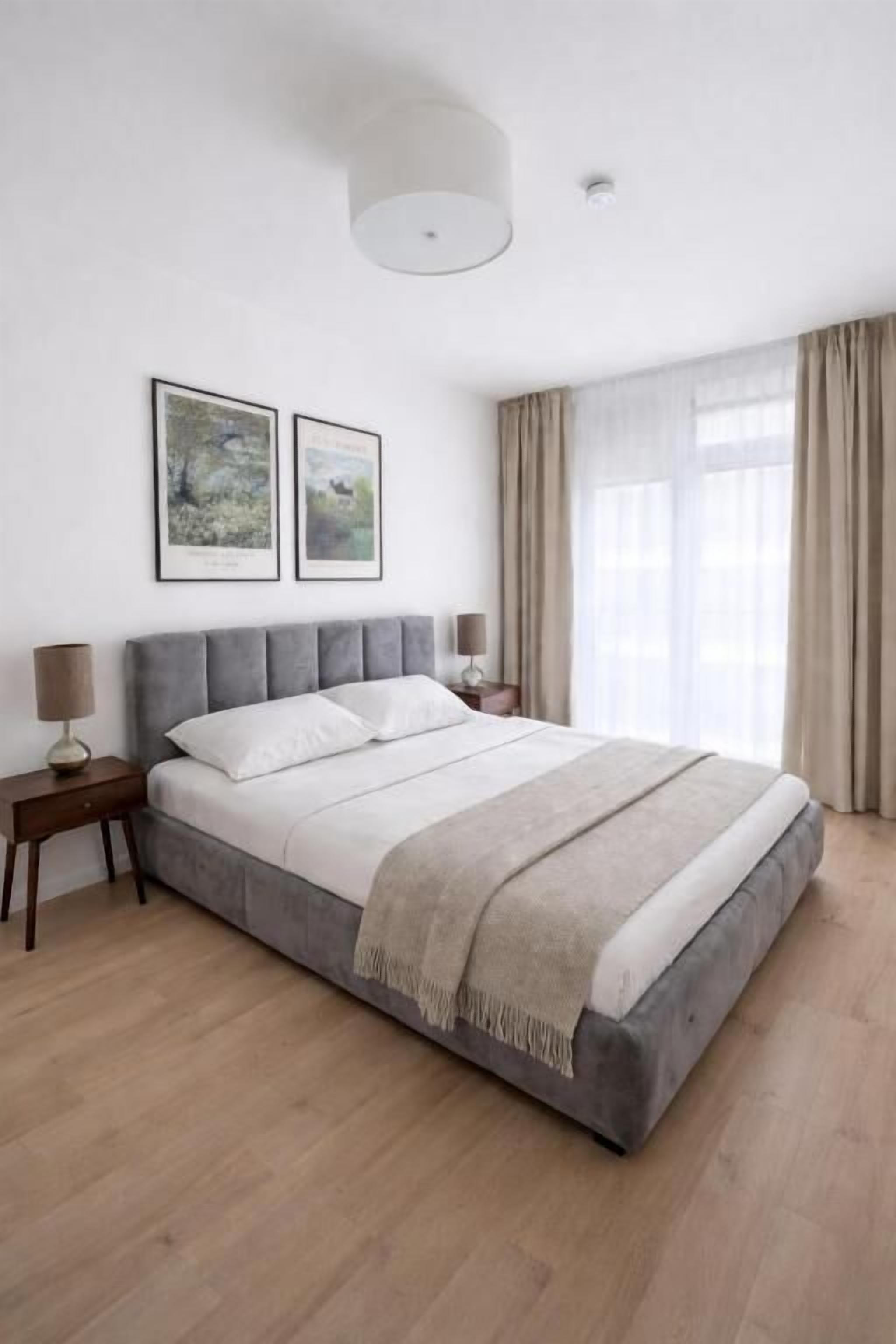 Ein Schlafzimmer mit einem großen Bett, zwei Nachttischen, einer Deckenleuchte und zwei gerahmten Bildern an der Wand.