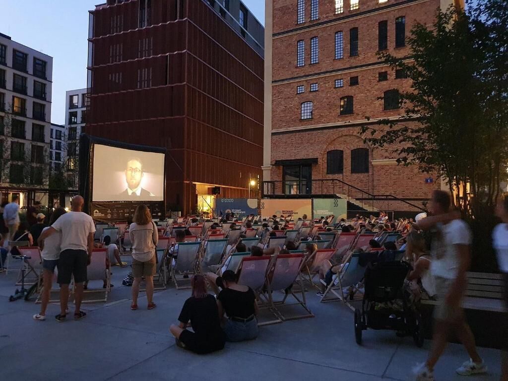 An outdoor cinema with a large screen and rows of seating.