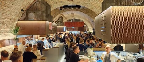 A bustling restaurant with a high, arched brick ceiling and a central bar area.