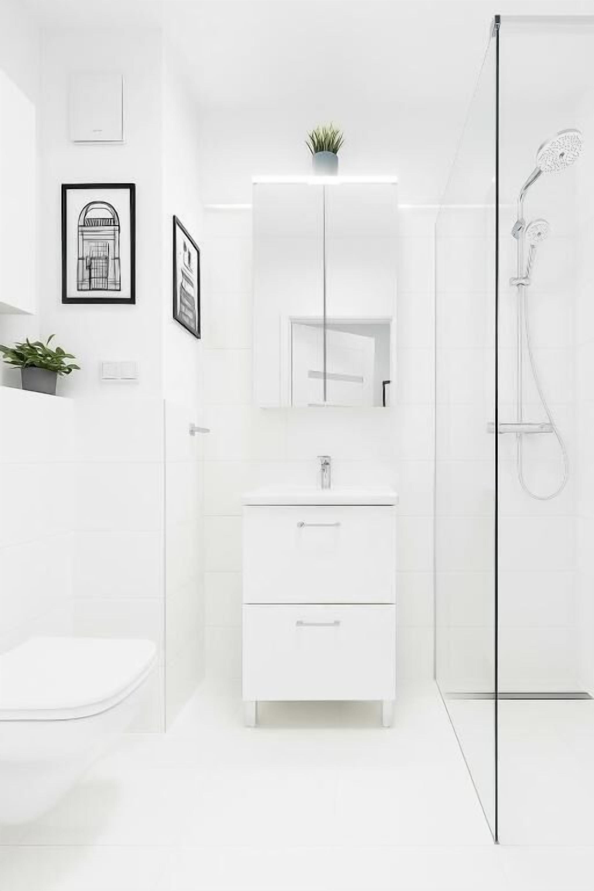 Un bagno moderno con un mobile lavabo bianco, cabina doccia in vetro e opere d'arte incorniciate alle pareti.